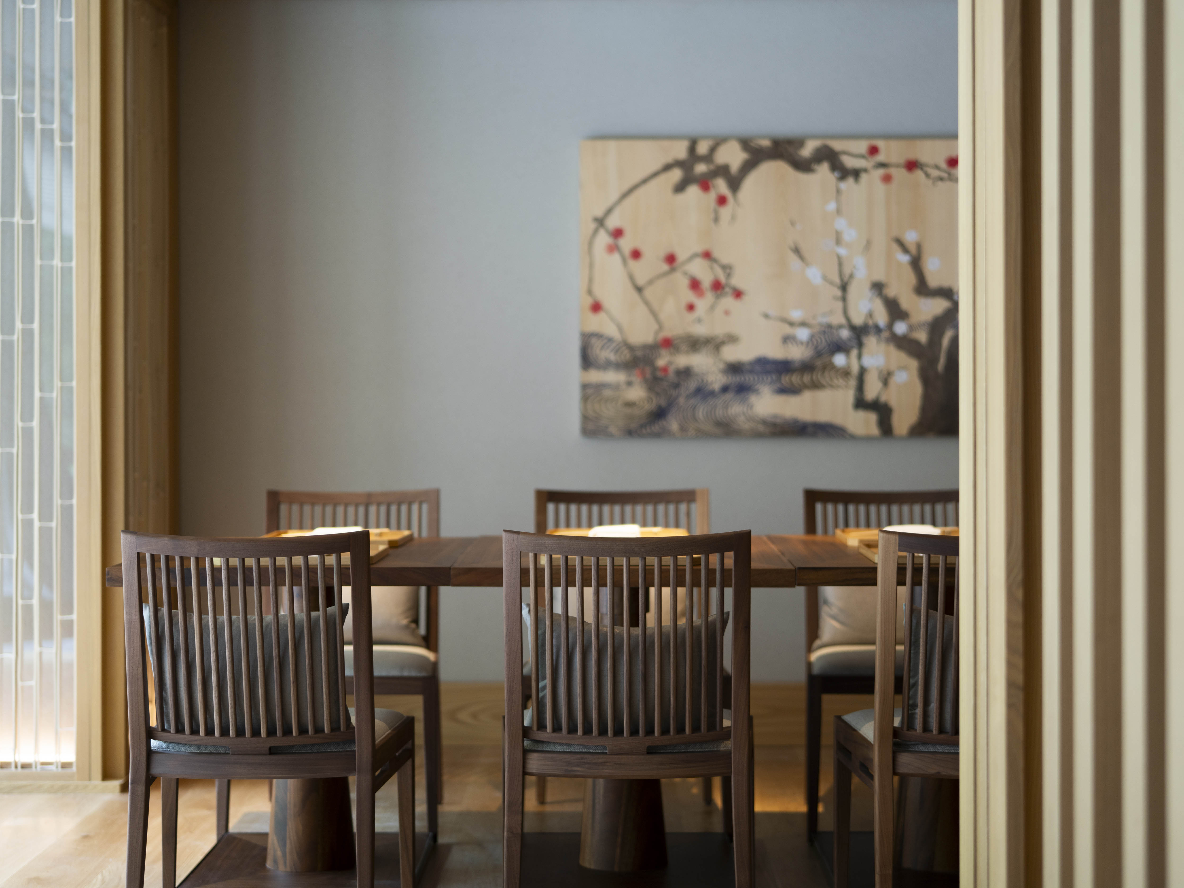Dining chairs surround a wooden table under a cherry blossom painting at Banyan Tree Higashiyama Kyoto.